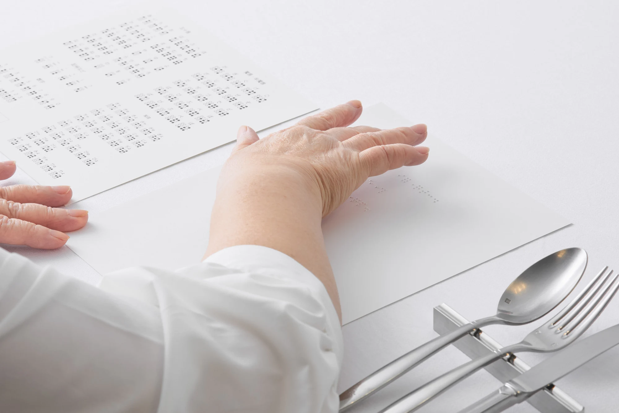 白いテーブルの上で、点字のメニューと点字の手紙に手を置いている